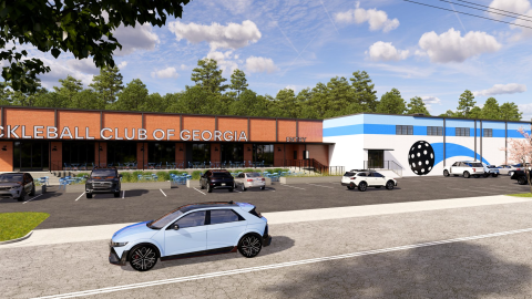 An image showing a large long warehouse building under blue skies near a wide street with pickleball courts and golf simulators and a bar inside.
