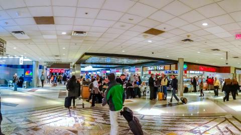 An image of a large and busy airport with many people hustling about near shops and eateries.