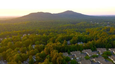 A photo of a green old mountain at sunset outside Atlanta Georgia surrounded by many tree and houses.