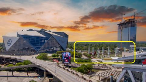 A photo of a large angular stadium and a tall glassy building under blue and orange skies and many roadways in Atlanta Georgia.