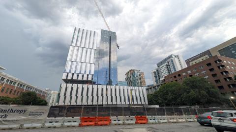 A photo of a large glassy new building in Midtown Atlanta under gray-blue skies near a wide street and many other buildings. 
