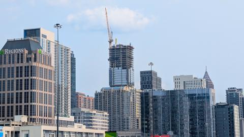 A photo of a new large and tall glassy skyscraper in Atlanta with a yellow crane and many tall buildings nearby, under hazy blue skies.