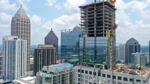 An aerial view of a large new glass and concrete building among many other tall structures in Midtown Atlanta, under blue skies.