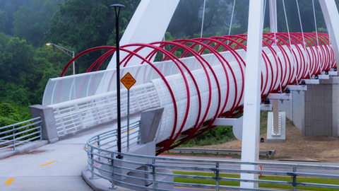 A large red and white pedestrian bridge spanning a busy highway in Atlanta near many trees.