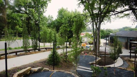 A large indoor and outdoor brewery space in an old building with many trees and patio areas beside a wide street near a retaining wall under hazy skies in Atlanta.