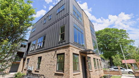 A photo of a large black and brick townhome unit on a large wide Atlanta street near green lawns.