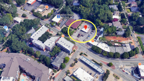 An overview of a parking lot and small building site in Kirkwood Atlanta along a wide road near many other buildings under blue skies.