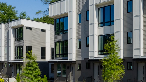 A large white gray and brown modern-style townhome in Atlanta under blue skies, with small trees in front and cozy contemporary interiors. 