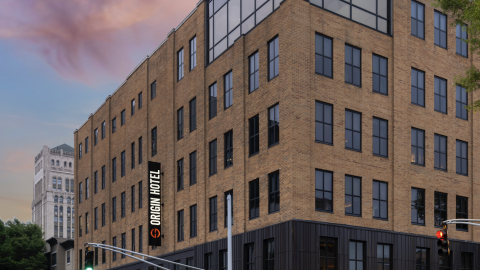 A photo of a large brick new hotel in downtown Atlanta under blue pink skies with modern artful interiors and high ceilings inside, plus a fancy restaurant with gold and black interiors.