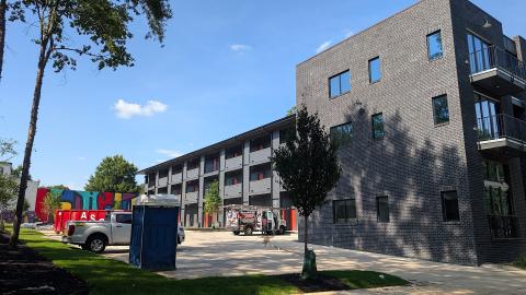 A black and brick large new building under blue skies in Atlanta near a wide street with many balconies. 