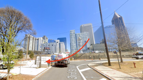A photo of a tunnel in Midtown Atlanta under a large highway and blue skies with many tall buildings around on all sides.