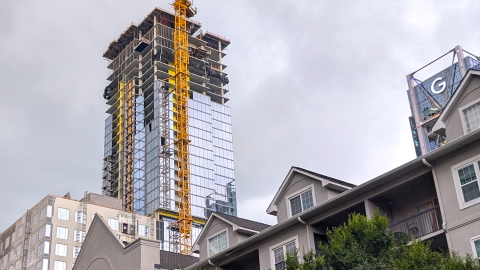 A photo of a large glassy tower with a yellow crane attached under gray skies near many tall buildings in Atlanta.