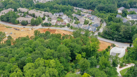 An aerial overview of a large new construction site beside many trees and new houses west of Atlanta, at a huge green park.