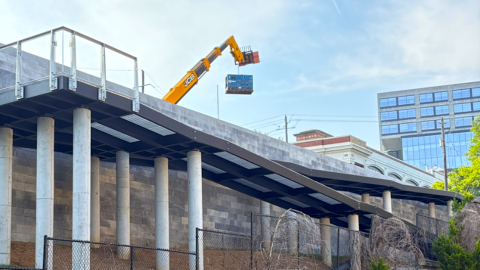 a new bridge structure leading to a wide concrete pathway near a large parking lot in Atlanta under blue skies.