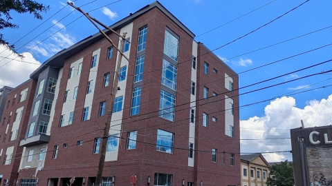 A photo of a parking lot site where a large brick and glass building has topped out with blue fencing around the base near the street in Atlanta.