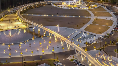 An image of a large new park with a long sweeping brick with many plazas and lights everywhere at night.