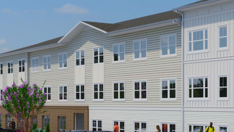 An image of a site for a large white and brick workforce housing build under blue skies near many wide streets in Atlanta.