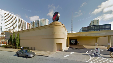 A photo of a bland beige building under blue skies with a round black sign on top. 