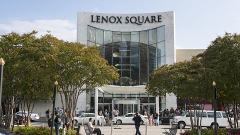 A photo of the exterior of a large mall with two stories of glass and many trees in front.