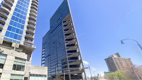A photo of a triangular high-rise in downtown Atlanta under blue skies near many wide streets, with other tall buildings nearby.