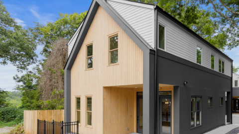 A large european-looking duplex property with wood on the exterior and gray and white walls and sleek modern interiors with white walls under many trees in Southeast Atlanta.