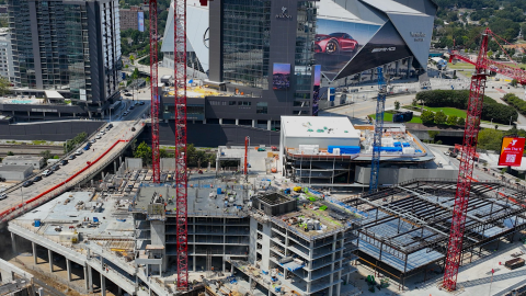 An aerial photo of a huge construction site near an angular Atlanta stadium with three red construction cranes and much construction activity all over. 