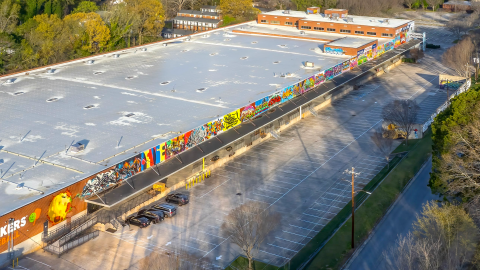 A photo of a large former factory in Atlanta near a wide parking lot with many trees around 