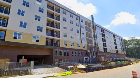 A photo of a large new affordable housing development near Atlanta under blue skies with many trees around.