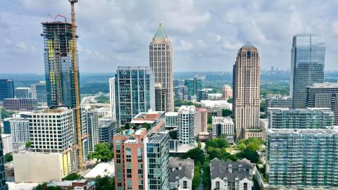 A photo of a large part of Midtown Atlanta under blue skies with many skyscrapers in the distance and many trees and streets around.