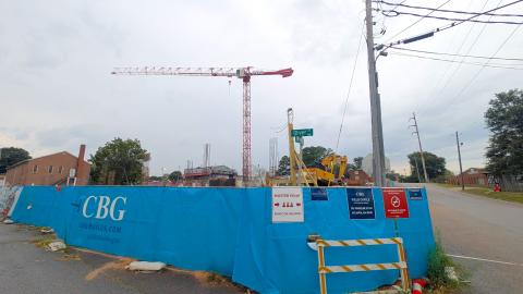 A photo of a large red crane over a construction site on Atlanta's Westside near two streets, with blue fencing around.