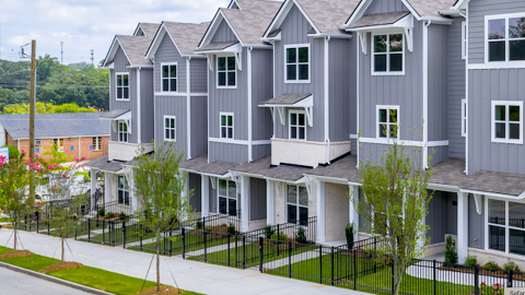 A row of traditional-style townhomes shown along a sloping street in Atlanta with a wide sidewalk in front and white modern interiors with many rooms.