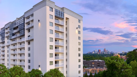 A photo of a large white building under blue and purples skies near many trees with hundreds of balconies in Atlanta.