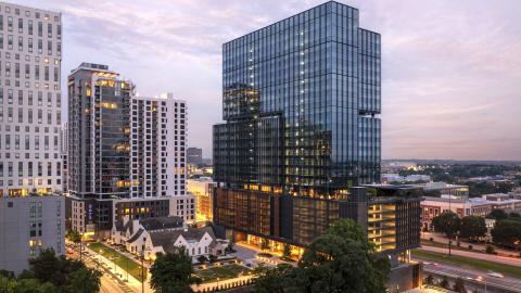 A photo of a large glassy new blue building in Midtown Atlanta with a new leafy rooftop restaurant and lounge under blue purple skies.