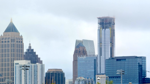 A photo of a large tall slender glassy new skyscraper rising over Atlanta, Georgia under many clouds.