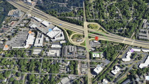 An overview of a large glassy and stone building under blue skies in Atlanta near a wide roadway and interstate. 