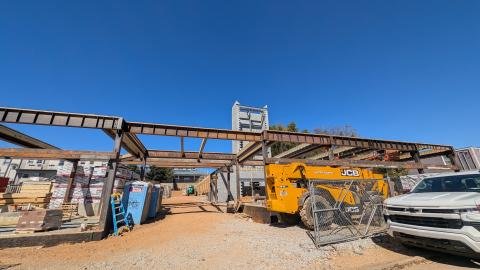 A photo of a large low building with steel and concrete and wood being build under clear blue October skies.