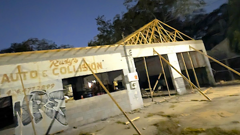 A photo of an old building being constructed into a new use with boards around concrete near a parking lot. 