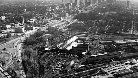 A historical photo of a huge industrial steel mill site in Atlanta near a huge freeway and city, beside railroad tracks.
