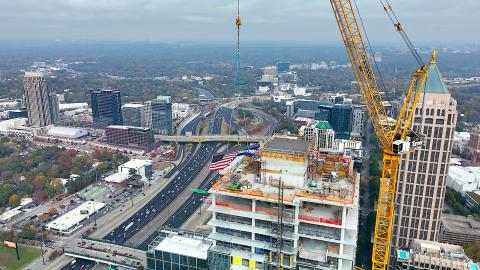 A photo of a large building with a yellow crane at top over Atlanta under hazy blue skies.
