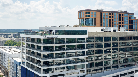 A photo of a large building with concrete and glass under blue and cloudy skies near a tan building in Atlanta.