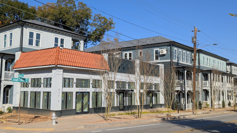 A photo of a new mix of storefronts and housing on a corner in English Avenue Atlanta under blue skies near two wide streets and a park. 
