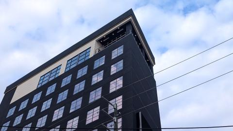 A photo of a tall black and beige hotel in downtown Atlanta with many square windows under blue cloudy skies. 
