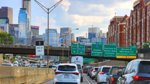 A photo of a large traffic jam in the middle of Atlanta with many cars stalled in the middle of many lanes near tall buildings. 