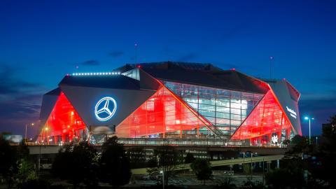 An image of a huge origami shaped stadium in Atlanta under blue dark skies near a wide elevated roadway.
