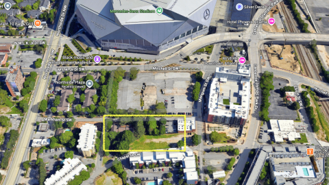 An image of a large angular football stadium with a big apartment complex of brick and glass and blue walls across the street, on a wide road in downtown Atlanta.