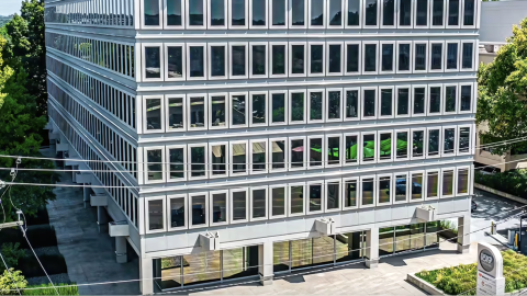A photo of a 1960s office building in the context of downtown Atlanta near a wide street with many trees and tall buildings around. 