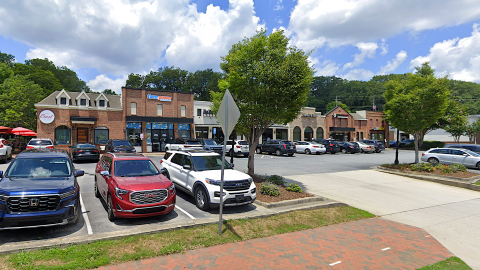 An image of a corner strip mall shopping center under blue skies in suburban Atlanta near wide streets.