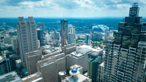 A photo of downtown Atlanta with many skyscrapers and a large stadium in the distance on a cloudy sunny day. 