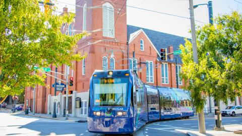 An image of a blue-purple trolley train in downtown Atlanta next to a brick church with overhead wires on a sunny day.