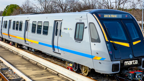 An image of a large new blue and gray MARTA train on tracks under a gray blue sky near many trees.